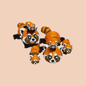 Peut inclure: Plusieurs figurines de pandas roux orange, blancs et bruns. Chaque figurine a une base noire et un visage détaillé. Certains pandas roux ont de plus petits pandas sur leur dos.