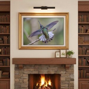 May include: A framed print of a hummingbird in flight, wings spread. The bird has iridescent green and blue feathers, with white accents on its tail. The artwork is displayed above a fireplace with a stone facade.