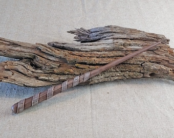 May include: A brown wooden wand with a dark brown, textured, and slightly raised design. The wand is decorated with runes.