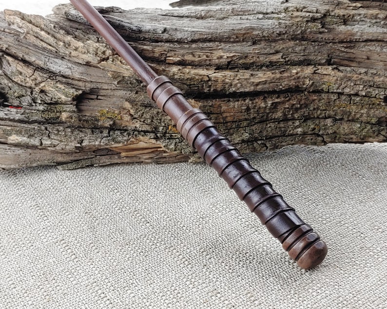 May include: A dark brown wooden wand with a textured grip and a rounded tip.