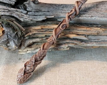 May include: A brown wooden wand with a vine and leaf design. The wand is carved with intricate details and has a natural, rustic look.
