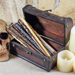 May include: A wooden treasure chest with a hinged lid, open to reveal a collection of wooden wands in various shades of brown, black, and white.
