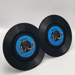 Può includere: Due ganci da parete in vinile nero con ganci color ottone. I dischi hanno etichette blu e bianche con il logo Philips e il numero 45. I ganci sono montati al centro dei dischi.