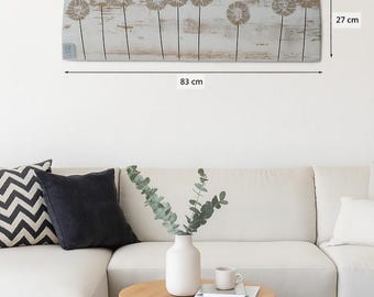 May include: A rectangular wooden wall art piece featuring a dandelion design. The artwork is 83 cm long and 27 cm high. The dandelions are in a light brown color against a white and light brown background. The artwork is mounted above a white sofa.