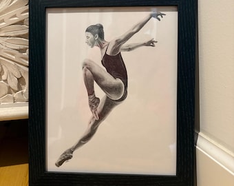 Puede incluir: Obra de arte enmarcada de una bailarina de ballet en el aire. La bailarina lleva un maillot rojo oscuro y zapatillas de punta. La obra de arte es en blanco y negro con un marco negro. La pose de la bailarina es elegante y dinámica.