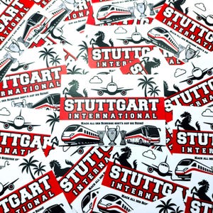 Op de afbeelding: Een verzameling rode en witte stickers met de tekst "STUTTGART INTERNATIONAL" en diverse reisgerelateerde afbeeldingen. De stickers bevatten afbeeldingen van vliegtuigen, treinen, palmbomen en een paard.