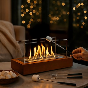Könnte beinhalten: Ein Tischkamin mit Holzsockel und Glasscheiben, der eine lebendige Flamme zeigt. Marshmallows werden über dem Feuer geröstet, mit Spießen und einer Schüssel mit Marshmallows in der Nähe. Der Hintergrund ist verschwommen mit warmen Lichtern.