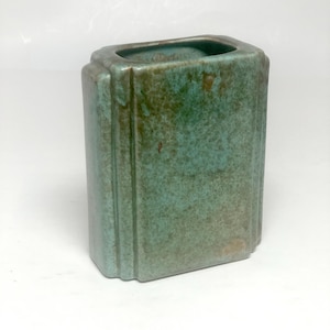 May include: A rectangular ceramic vase with rounded corners and vertical ribbed detailing along the sides. The surface features a mottled glaze in shades of teal, turquoise, and earthy brown, creating a textured appearance with a glossy finish.