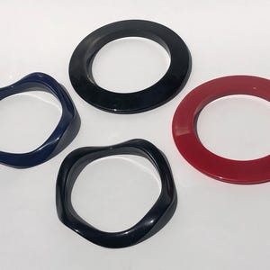 May include: Four colorful bangles in navy blue, black, and red. Two have a wavy design, while the other two are smooth and circular. These accessories are perfect for adding a pop of color to any outfit.