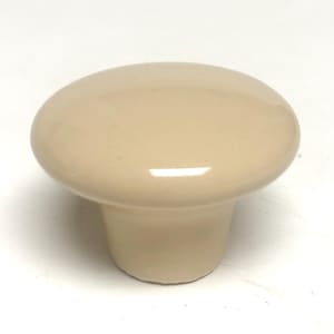 May include: A solid, light beige cabinet knob with a smooth, glossy finish. The knob features a rounded, mushroom-shaped top that tapers down into a cylindrical base. The surface is uniform in color and reflects light, showing a clean, simple design.