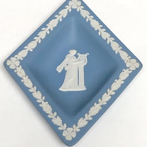 May include: A blue diamond-shaped dish with a white relief design. The dish features a white border of leaves and flowers. In the center is a white figure playing a harp. The dish is likely made of ceramic.