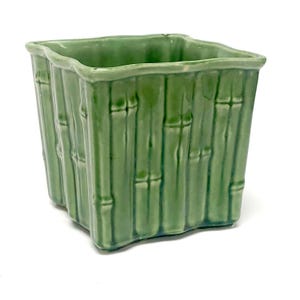 May include: A square ceramic planter with a glossy light green glaze. The exterior surface features a molded relief pattern that mimics the segmented appearance of bamboo stalks, with vertical ridges and nodes around the entire perimeter.