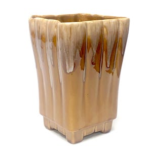 May include: A square ceramic vase featuring a glossy finish with a vertical ribbed texture. The glaze transitions from a deep caramel brown at the base to a lighter, creamy beige drip pattern near the top rim, supported by four small feet.