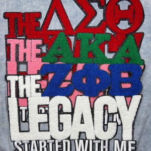 May include: Close-up of a light blue fabric with colorful text. The text includes the phrases "THE," "LEGACY," and "STARTED WITH ME." The letters are in red, green, blue, pink, and white, with a textured, fuzzy appearance.