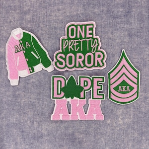 May include: A collection of embroidered patches in pink, green, and white. The patches include a jacket, a military rank insignia, and text that reads "ONE PRETTY SOROR" and "DOPE AKA".