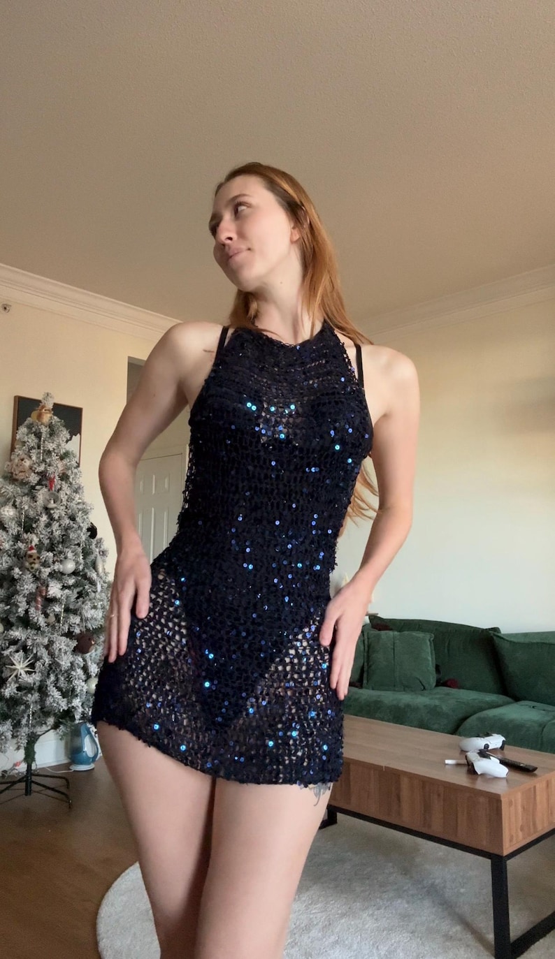 May include: A black halter dress with a mesh design and sparkling sequins. The dress is sleeveless and has a mini length. The dress is worn over a black undergarment. The dress is a part of the clothing category.
