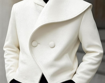 May include: A white, textured jacket with a unique collar design and two large, round buttons. The jacket has a wrap-style closure and a small pocket. The sleeves are long, and the jacket appears to be made of a leather-like material.