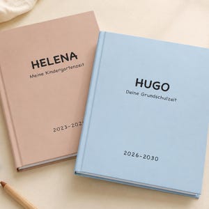 Può includere: Due libri di ricordi con copertina rigida opaca. Il libro rosa polvere riporta il nome HELENA, il testo Meine Kindergartenzeit e 2023-2024. Il libro azzurro riporta il nome HUGO, il testo Deine Grundschulzeit e 2026-2030.