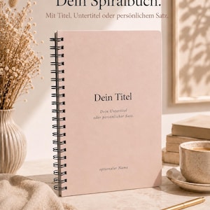 May include: A light pink spiral-bound notebook with black wire binding. The cover features the printed text "Dein Spiralbuch. Mit Titel, Untertitel oder persönlichem Satz." followed by "Dein Titel", "Dein Untertitel oder persönlicher Satz.", and "optionaler Name".