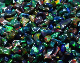 May include: A pile of polished black opal gemstones with vibrant flashes of color. The opals display a range of hues, including green, blue, red, and yellow, creating a dazzling display. The gemstones are irregularly shaped and have a glossy finish.