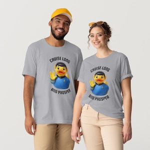 Puede incluir: Dos personas con camisetas grises con un diseño de pato de goma. El pato viste un uniforme de Star Trek y el texto dice "Cruise Long and Prosper". Una persona lleva una gorra de béisbol amarilla.