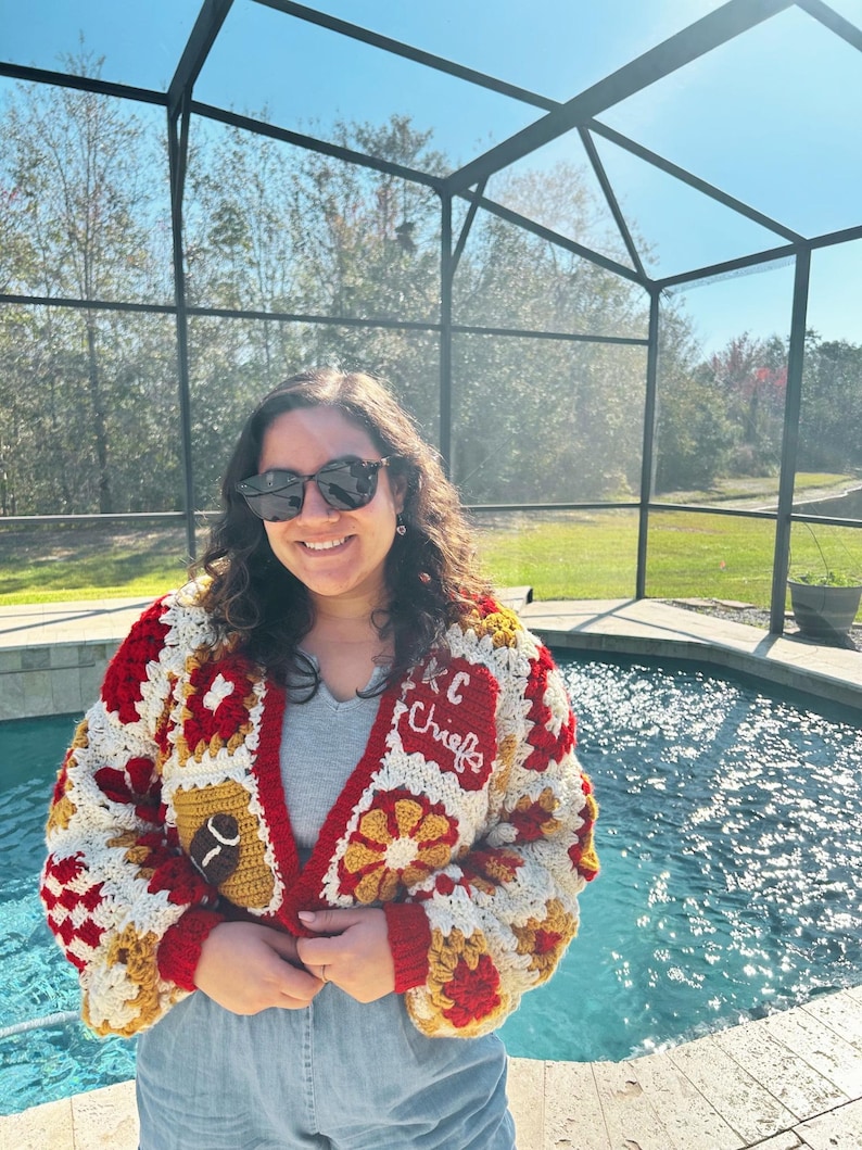 May include: A handmade crochet cardigan in red, white, and gold, featuring a football and the text "KC Chiefs". The cardigan has a V-neck and is made with a granny square pattern. The sleeves and trim are red.