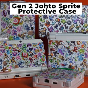 Puede incluir: Una colección de fundas protectoras blancas para consolas de juegos portátiles con un patrón denso y colorido de varios sprites de pequeñas criaturas. El texto Gen 2 Johto Sprite Protective Case está impreso en negro sobre un fondo rectangular blanco.