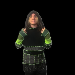 May include: Black hooded sweatshirt with neon green stitching and accents. The sleeves are green and black with neon green trim. The bottom of the sweatshirt has a black sequined trim. The person is wearing black pants.