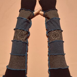 May include: A pair of patchwork arm warmers in shades of black, grey, and blue, with a decorative floral pattern. The edges are trimmed with blue stitching. The top section features black fabric with grey stripes. The arm warmers are designed to cover the arms.