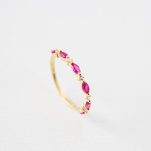 Peut inclure: Une bague en or ornée d'une série de pierres précieuses roses en forme de marquise et de petits diamants étincelants. Le corps de la bague est en or poli, et les pierres sont serties dans un motif délicat et répété.