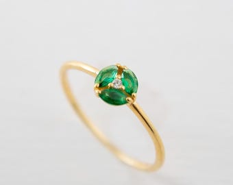 Puede incluir: Un delicado anillo de oro con un grupo de tres esmeraldas de corte ovalado y un pequeño diamante. El anillo tiene una banda fina y pulida. Las esmeraldas son de un verde vibrante, el diamante está en el centro.