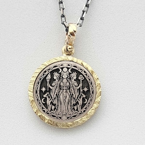 May include: A round pendant necklace featuring a three-faced figure holding a torch and a key, flanked by two dogs. The central design is silver-toned with a dark background, surrounded by a textured gold-toned border and a silver chain.