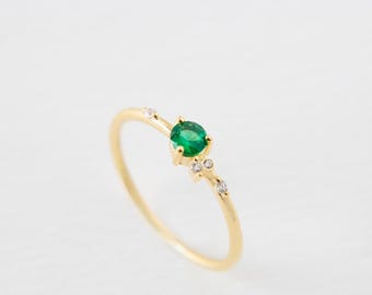 Puede incluir: Un delicado anillo de oro con una vibrante gema verde como punto focal. El anillo está adornado con pequeñas piedras brillantes. El diseño es simple pero elegante, perfecto para el uso diario o ocasiones especiales.