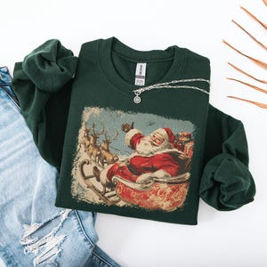 dark-green Christmas sweatshirt with vintage 60s Santa Claus riding sleigh and reindeer illustration; retro Santa Christmas sweater, classic holiday sweatshirt, cozy winter pullover, nostalgic Christmas design, unisex festive apparel, holiday gift idea, traditional Christmas aesthetic sweatshirt, matching family Christmas outfits.