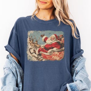 blue Christmas comfort colors shirt with vintage 60s Santa Claus riding sleigh and reindeer illustration; retro Santa Christmas tee, classic holiday t-shirt, cozy winter top, nostalgic Christmas graphic design, unisex festive crewneck, holiday gift idea, traditional Christmas aesthetic sweatshirt, matching family Christmas outfits sweater.