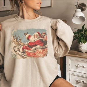 sand beige Christmas sweatshirt worn by a woman with vintage 60s Santa Claus riding sleigh and reindeer illustration; retro Santa Christmas sweater, classic holiday sweatshirt, cozy winter pullover, nostalgic Christmas design, unisex festive apparel, holiday gift idea, traditional Christmas aesthetic sweatshirt, matching family Christmas outfits.