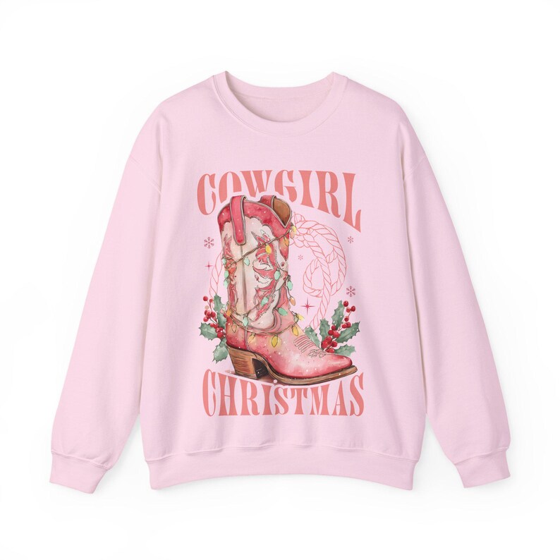 pink Sweatshirt with Western Christmas graphic design featuring a pink cowgirl boot wrapped in holiday lights, holly berries, rope lasso graphic, and text "Cowgirl Christmas"; festive Western holiday sweatshirt, country Christmas sweater, cowgirl aesthetic clothing, cozy winter pullover, Western Christmas gift, farmhouse holiday outfit, country girl Christmas apparel.