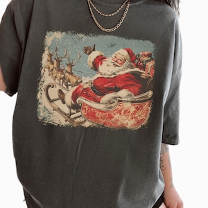 pepper dark-grey Christmas comfort colors shirt with vintage 60s Santa Claus riding sleigh and reindeer illustration; retro Santa Christmas tee, classic holiday t-shirt, cozy winter top, nostalgic Christmas graphic design, unisex festive crewneck, holiday gift idea, traditional Christmas aesthetic sweatshirt, matching family Christmas outfits sweater.