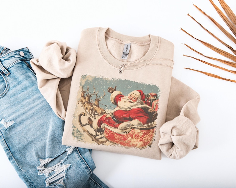 sand beige Christmas sweatshirt with vintage 60s Santa Claus riding sleigh and reindeer illustration; retro Santa Christmas sweater, classic holiday sweatshirt, cozy winter pullover, nostalgic Christmas design, unisex festive apparel, holiday gift idea, traditional Christmas aesthetic sweatshirt, matching family Christmas outfits.