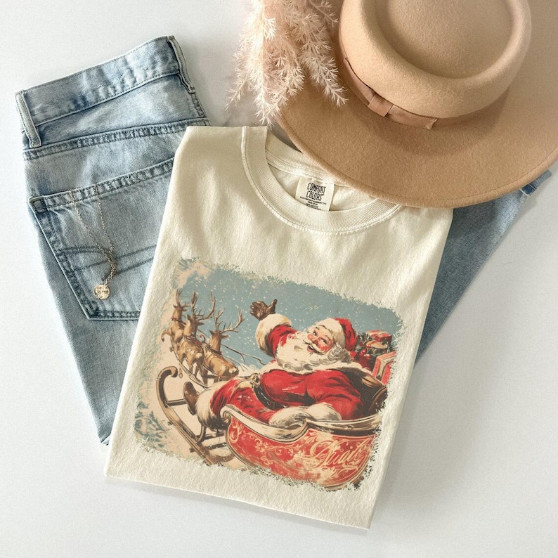 ivory Christmas comfort colors shirt with vintage 60s Santa Claus riding sleigh and reindeer illustration; retro Santa Christmas tee, classic holiday t-shirt, cozy winter top, nostalgic Christmas graphic design, unisex festive crewneck, holiday gift idea, traditional Christmas aesthetic sweatshirt, matching family Christmas outfits sweater.