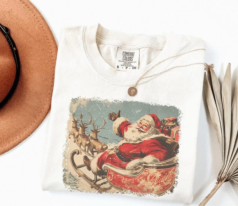 ivory Christmas comfort colors shirt with vintage 60s Santa Claus riding sleigh and reindeer illustration; retro Santa Christmas tee, classic holiday t-shirt, cozy winter top, nostalgic Christmas graphic design, unisex festive crewneck, holiday gift idea, traditional Christmas aesthetic sweatshirt, matching family Christmas outfits sweater.