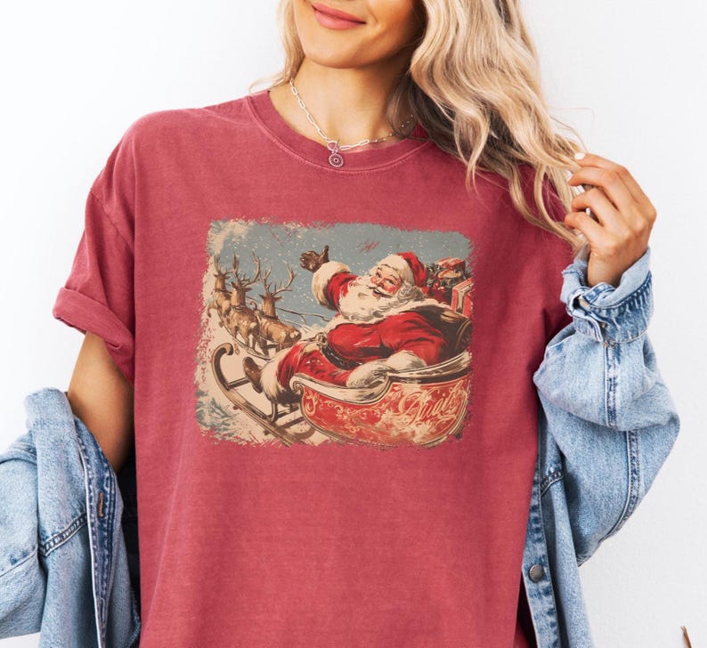 red crimson Christmas comfort colors shirt with vintage 60s Santa Claus riding sleigh and reindeer illustration; retro Santa Christmas tee, classic holiday t-shirt, cozy winter top, nostalgic Christmas graphic design, unisex festive crewneck, holiday gift idea, traditional Christmas aesthetic sweatshirt, matching family Christmas outfits sweater.