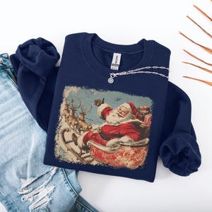 dark-blue Christmas sweatshirt with vintage 60s Santa Claus riding sleigh and reindeer illustration; retro Santa Christmas sweater, classic holiday sweatshirt, cozy winter pullover, nostalgic Christmas design, unisex festive apparel, holiday gift idea, traditional Christmas aesthetic sweatshirt, matching family Christmas outfits.