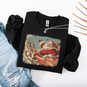 black Christmas sweatshirt with vintage 60s Santa Claus riding sleigh and reindeer illustration; retro Santa Christmas sweater, classic holiday sweatshirt, cozy winter pullover, nostalgic Christmas design, unisex festive apparel, holiday gift idea, traditional Christmas aesthetic sweatshirt, matching family Christmas outfits.