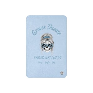 Pu&ograve; includere: Una coperta rettangolare azzurra con una grafica centrale raffigurante un teschio con un'acconciatura a chignon spettinato e occhiali da sole blu. Il testo recita Graves Disease, Faking Wellness e Every Single Day in blu.