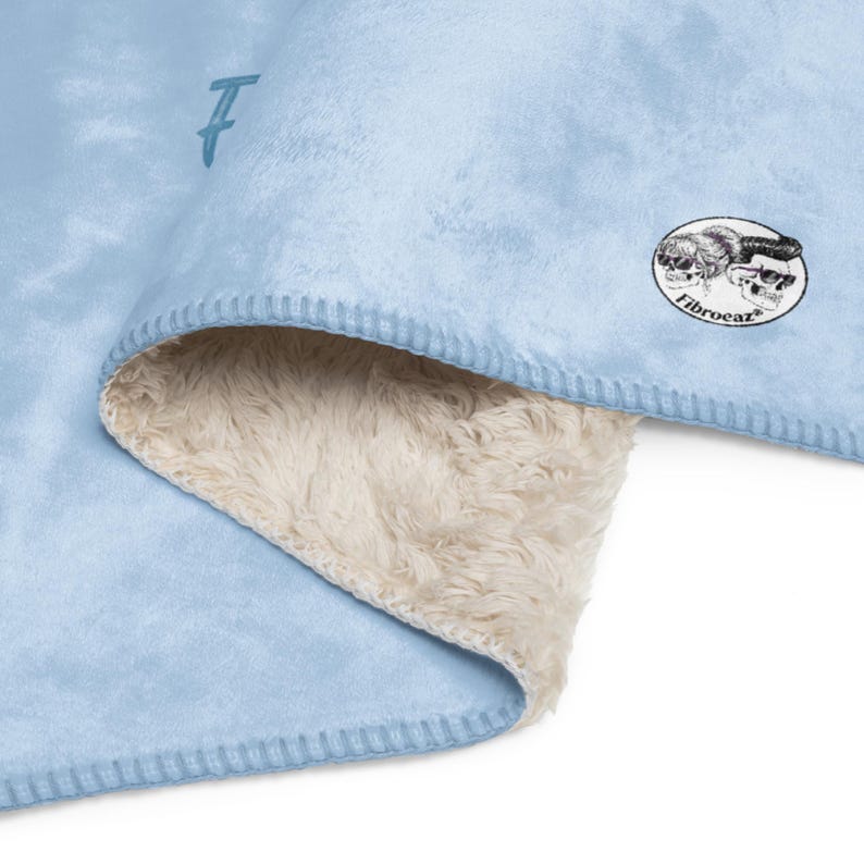 Pu&ograve; includere: Una coperta azzurra con una morbida fodera in finta pelle di pecora color crema. La coperta presenta una toppa circolare con una grafica in bianco e nero di due teschi con occhiali da sole e il testo Fibroeaz, oltre a un piccolo logo F.