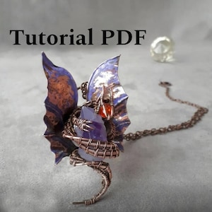 Puede incluir: Colgante de dragón hecho a mano con alambre de cobre, amatista y un pequeño cristal naranja. El dragón tiene alas moradas y cobrizas y está sujeto a una cadena. El texto "Tutorial PDF" está en la parte superior.