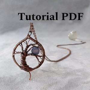 May include: Copper-colored wire pendant necklace in the shape of a tree, with a blue-grey stone at the center. The pendant hangs from a delicate chain. The words "Tutorial PDF" are printed in black above the pendant.