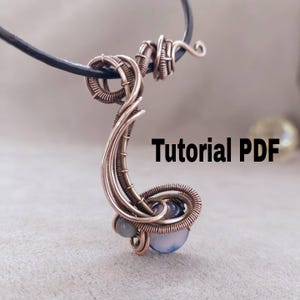 May include: A copper-colored wire-wrapped pendant with a curved design, featuring a blue and gray gemstone. The pendant hangs from a black leather cord. The text "Tutorial PDF" is displayed in black.