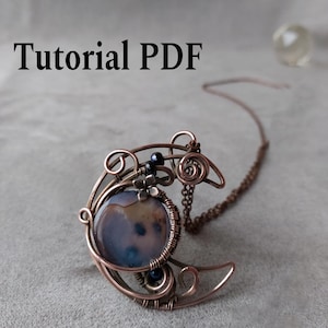 Puede incluir: Un colgante de alambre de color cobre en forma de media luna, con una piedra grande, redonda, azul y marrón. El colgante tiene remolinos decorativos y pequeñas cuentas negras. El texto "Tutorial PDF" está en la esquina superior izquierda.